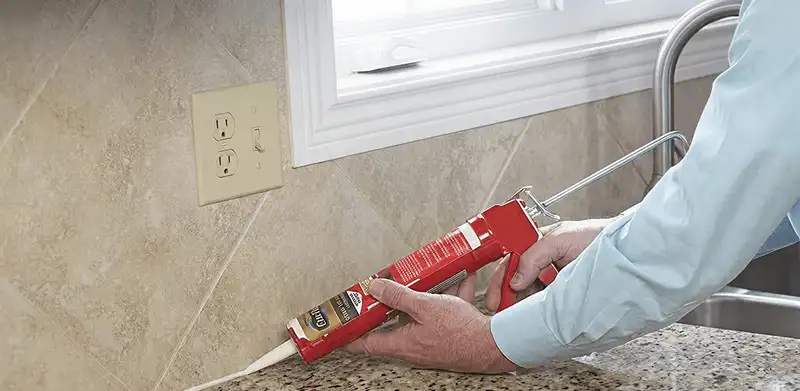 Handyman applying caulk along a kitchen backsplash and countertop seam in Albuquerque, NM